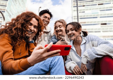 Group of young gen z friends sitting together in the city using cell phone app to share funny content 商業照片 © 