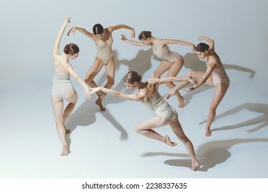Group of young girls, ballet dancers performing, posing isolated over grey studio background. Circle movements. Concept of art, beauty, aspiration, creativity, classic dance style, elegance