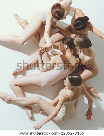 Group of young girls, ballet dancers performing, posing isolated over grey studio background. Art of classics. Concept of art, beauty, aspiration, creativity, classic dance style, elegance