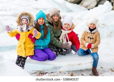 Group Of Young Girls Sitting At The Ice Block On The Frozen Lake. Outdoors