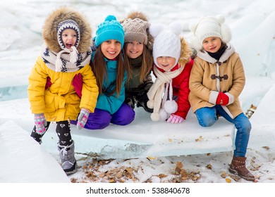 Group Of Young Girls Sitting At The Ice Block On The Frozen Lake. Outdoors