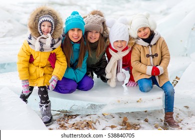 Group Of Young Girls Sitting At The Ice Block On The Frozen Lake. Outdoors