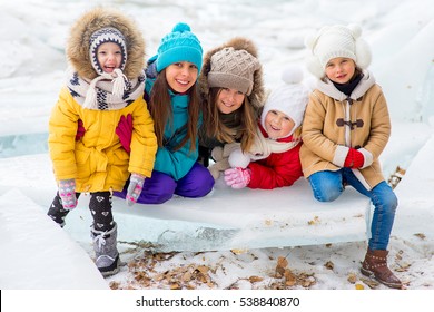 Group Of Young Girls Sitting At The Ice Block On The Frozen Lake. Outdoors