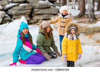 Group Of Young Girls Sitting At The Ice Block On The Frozen Lake. Outdoors