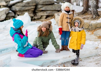 Group Of Young Girls Sitting At The Ice Block On The Frozen Lake. Outdoors