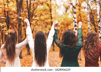 Group of young girls standing together holding hands in park, raise their hands up
