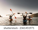 Group of young happy kayakers are having fun in winner poses at sunset sea bay
