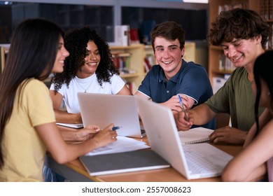 Group of young high school students doing classwork together using laptop sitting in library. Happy diverse Generation z classmates meeting brainstorming studying with computers and notebooks - Powered by Shutterstock