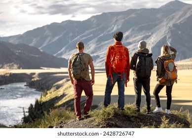 Group of young hikers with backpacks are standing at observation point in mountains and enjoying nice view at sunset and big river - Powered by Shutterstock