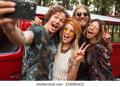 Group of young hippy men and women smiling and taking selfie on mobile phone near vintage minivan into the nature - Powered by Shutterstock