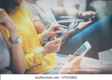 Group of young hipsters sitting on sofa holding en hands and using digital tablet,smartphone.Coworking team concept.Horizontal,blurred background