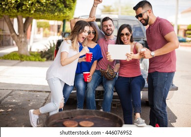 Group of young Hispanic friends tailgating and watching a baseball game on the back of a pick up truck with a tablet computer and supporting their team - Powered by Shutterstock