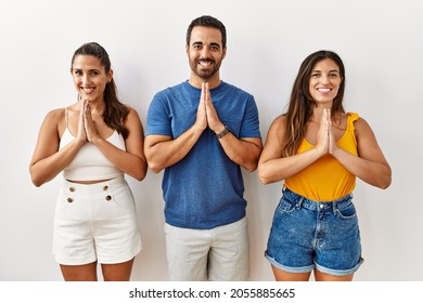 Group Of Young Hispanic People Standing Over Isolated Background Praying With Hands Together Asking For Forgiveness Smiling Confident. 