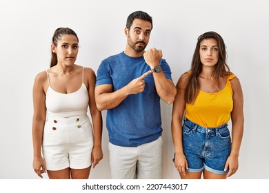 Group Of Young Hispanic People Standing Over Isolated Background In Hurry Pointing To Watch Time, Impatience, Looking At The Camera With Relaxed Expression 