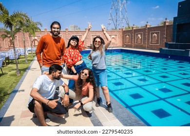 Group of young indian friends having fun standing at pool side resort in hot sunny day. Summer holiday and vacation concept.