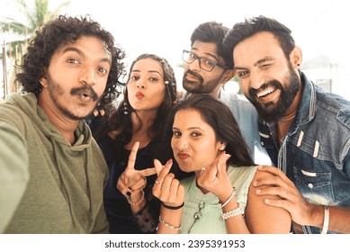 Group of young Indian friends taking selfie with grimacing faces by looking camera during reunion party - concept of friendship bonding, zen z lifestyle and social media sharing - Powered by Shutterstock