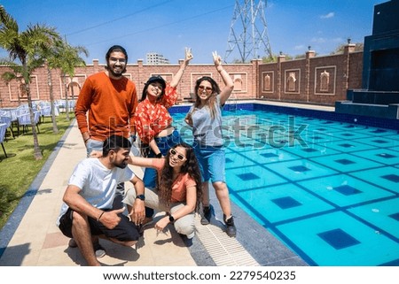 Group of young indian Zen Z friends having fun standing at pool side resort in hot sunny day. Summer holidays and vacations concept. 
