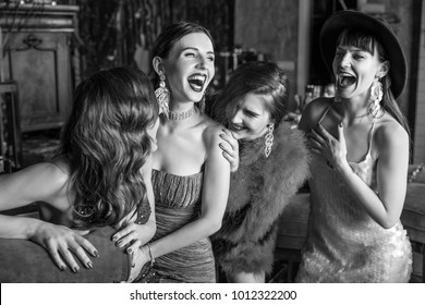 Group Of Young Laughing Stylish Girls Dressed Classical Style In Interior Of Luxury Club. Black-white Photo.