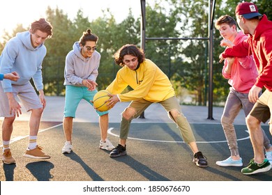 Group Of Young Male Teenagers In Colourful Hoodies Playing Basketball Outdoors In The Street