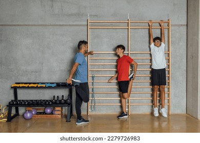 Group of young man teenagers relaxing stretching and having a break on the wooden gymnastics wall bars in gym, in dark light, night. Horizontal, frontal view copy-space - Shutterstock ID 2279726983