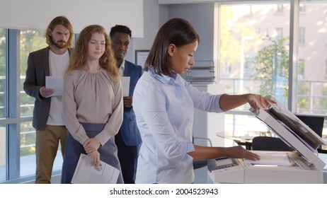 Group of young managers standing in queue for copier at office. Multiethnic colleagues standing in line waiting to use copier machine in modern workplace