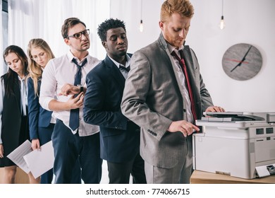 group of young managers standing in queue for copier at office