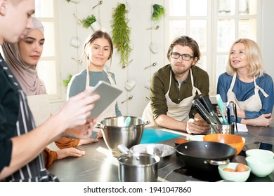 Group Of Young And Mature People Interested In Cooking Looking At Male Coach With Digital Tablet And Listening To Him During Master Class