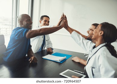 Group of young medical specialists team high five over table as for raising team spirit, sitting in front of each other and smiling