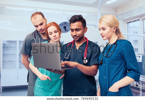 A group of young medical\
students with mixed-race surgeons examining these operations in a\
laptop.