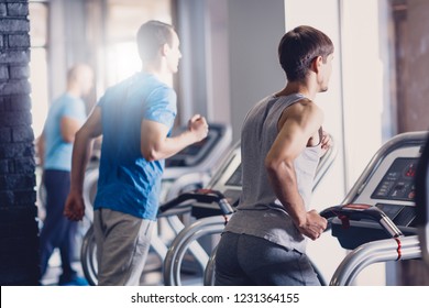 A Group Of Young Men Doing Jogging On A Treadmill. Joint Exercise In The Gym To Improve Physical Fitness. Men's Sportswear For Sports. Group Sports With A Beautiful View From The Window