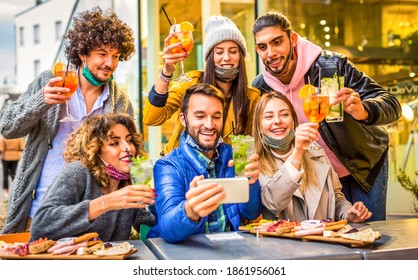 group of young millennial friends making a toast while making a selfie celebrating christmas wearing warm winter clothes.students having fun in a  outdoors open bar at sunset. friendship and life