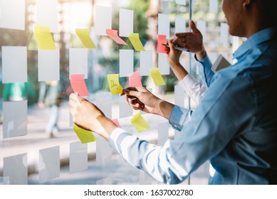 Group Of Young Modern Business People Planning And Brainstorming Putting Sticky Notes On Glass Wall In The Office.