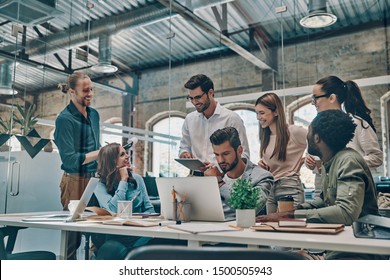 Group Of Young Modern People In Smart Casual Wear Communicating And Using Modern Technologies While Working In The Office                 