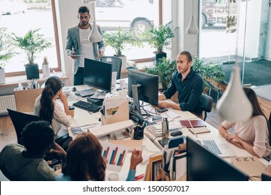 Group of young modern people in smart casual wear communicating and using modern technologies while working in the office           