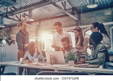 Group of young modern people in smart casual wear communicating and using modern technologies while working in the office - Shutterstock ID 1557471698