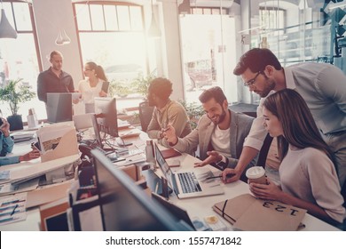Group of young modern people in smart casual wear communicating and using modern technologies while working in the office - Shutterstock ID 1557471842