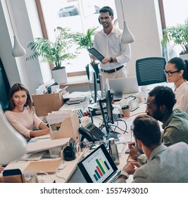 Group of young modern people in smart casual wear communicating and using modern technologies while working in the office - Shutterstock ID 1557493010