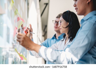 Group of young modern people in smart casual wear planning and brainstorming putting sticky notes on glass wall in the office.