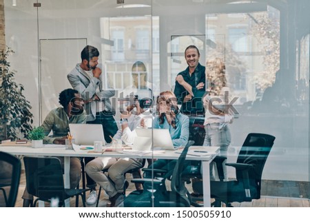 Group of young modern people in smart casual wear communicating and using modern technologies while working in the office        