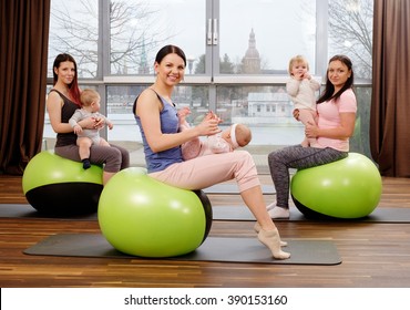 Group Of Young Mothers And Their Babies Doing Yoga Exercises On Gymnastic Balls At Fitness Studio.