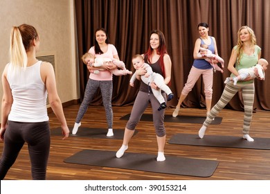 Group Of Young Mothers And Their Babies Doing Yoga Exercises On Rugs At Fitness Studio.