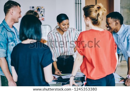Group of young multicultural people in casual wear laughing during colaboration on design project in modern coworking space.Team of cheerful hipster students having fun during common task