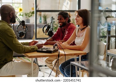 Group of young multicultural people sitting by desk in studio in front of each other and recording their conversation or discussion - Powered by Shutterstock