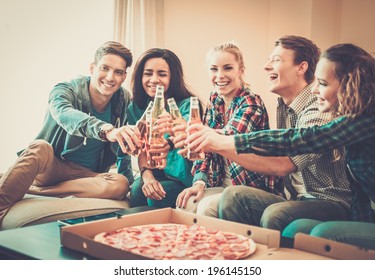 Group Of Young Multi-ethnic Friends With Pizza And Bottles Of Drink Celebrating In Home Interior