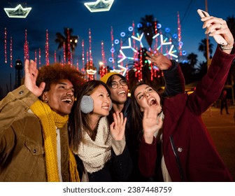 Group of young multiethnic friends in winter clothes making a selfie or video call during the night at a Christmas fair - Powered by Shutterstock