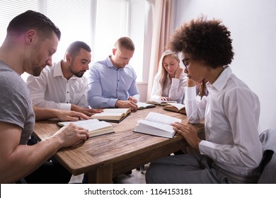 Group Of Young Multiethnic People Reading Bible Over Wooden Desk
