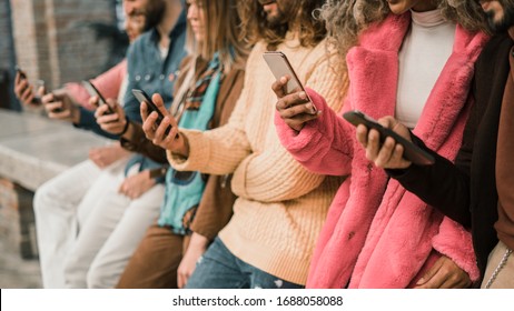 Group of young multi-ethnic people using smartphone sitting in a bench. Multiracial people holding smart mobile phones and watching their screen outdoors. - Shutterstock ID 1688058088