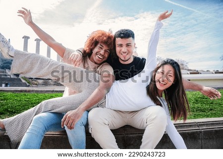 A group of young multiracial people having fun together. Three mixed teenagers smiling looking at camera. One asian woman spreading on top of her friends. Diverse students bonding on a social meeting