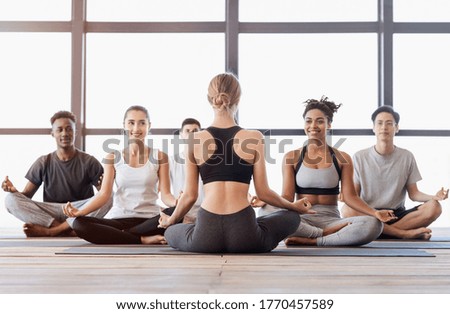Group of young multiracial people practicing yoga with instructor in modern light studio, free space