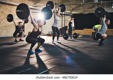 Group of young muscular adult male and females lifting large barbells in cross-fit class with thick mats and brick walls - Powered by Shutterstock